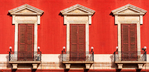 old red facade of house with three brown vintage wooden windows in retro italian european style