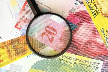 Swiss franc banknotes and magnifying glass. The current francs money bills with loupe lies on table