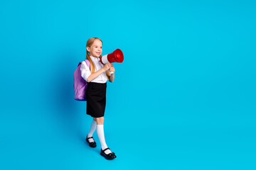 Young schoolgirl with megaphone in school uniform smiling cheerfully against a blue background, promoting education