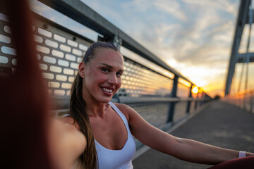Smiling woman taking a selfie on a bridge during sunset. The scene captures a moment of relaxation...