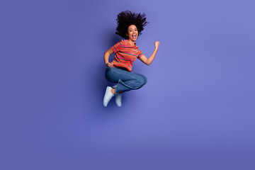 Young woman jumping joyfully in casual outfit with vibrant purple background showing happiness and...