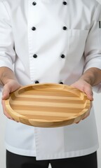 Unrecognizable chef in a white uniform with black buttons presents an empty round bamboo plate. He holds the natural wooden dish forward against a clean white background, perfect fo