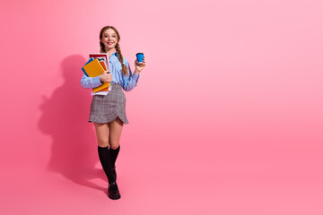 Happy young student holding book and coffee, smiling on pink background, depicting education and...