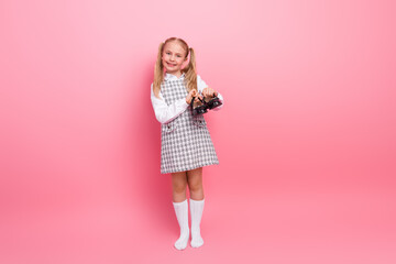 Charming young schoolgirl holding a vintage camera against a pink background, showcasing cute style