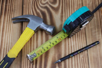 Workshop tools on oak wood board with retractable tape measure and claw hammer along carpenter...