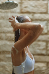 woman showering outdoors with soap suds on skin, natural stone wall background, wet hair, morning hygiene routine, fresh and relaxing atmosphere