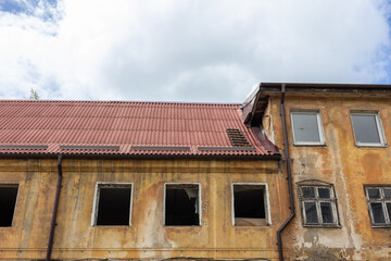Old building with red tile roof and broken windows. Weathered facade with peeling paint and visible...