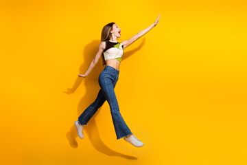 Joyful young woman jumping against a vibrant yellow wall expressing excitement and dynamism with...