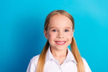 Cheerful young schoolgirl on blue background wearing white shirt with ponytails showcasing a bright and happy smile