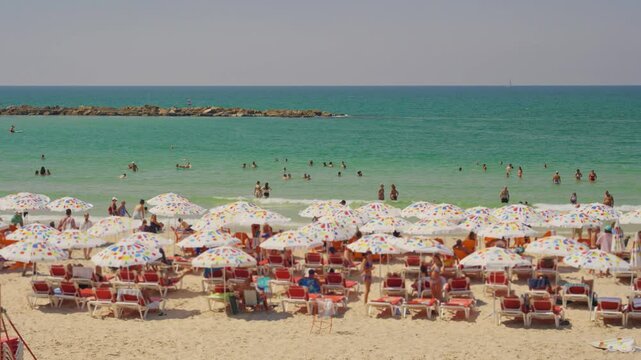 Wide shot on Tel Aviv beach coastline with sun umbrellas and people bathing. Hot summer day outdoors in Israel. Tourists and locals visit mediterranean sea. Enjoying a swim in water by sandy shores