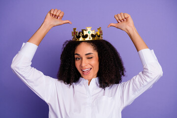 Young woman wearing a crown giving a playful gesture on a vibrant purple background
