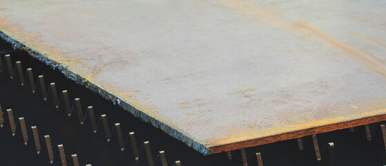 A brownish colored metal sheet is placed on the surface. The plate is made of metal and has a rough texture. It is placed on the black tabletop of the laser plasma cutting machine