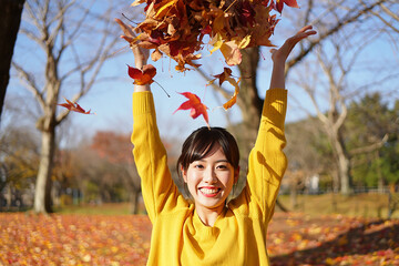 Joyful young woman in yellow sweater throwing colorful autumn leaves in the air