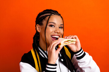 Young woman enjoying a fresh sandwich, showcasing casual style and happiness on an orange...