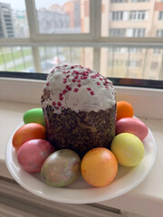 Easter cake in sugar glaze and painted eggs on a white plate on a windowsill, close-up