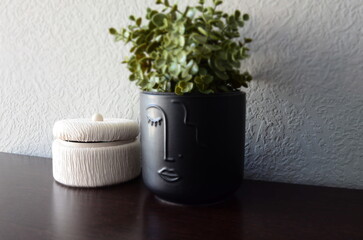 Black face planter with a plant and a decorative container on a wooden surface
