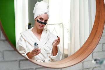 Woman applying under-eye patches in a bright, relaxing bathroom setting during daytime