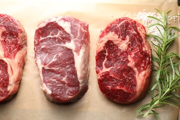 Pieces of raw beef meat, rosemary and salt on parchment paper, above view