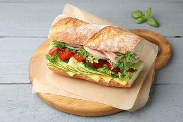 Tasty baguette sandwich with ham, cheese and vegetables on grey wooden table, closeup