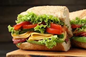 Pieces of tasty baguette sandwich with smoked sausage, cheese and vegetables on wooden board...
