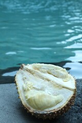 Fresh ripe durian on stone surface near swimming pool outdoors, closeup