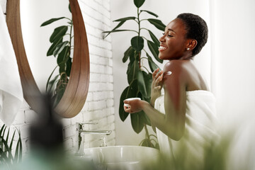 Woman applying lotion and enjoying self-care in a bright bathroom with plants and a large mirror
