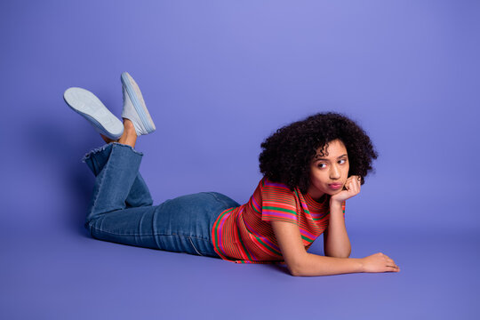 Young woman wearing casual colorful t-shirt and jeans, lying on purple background, looking thoughtful, fashion concept
