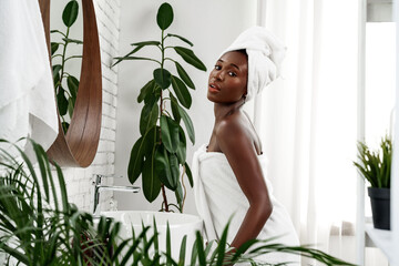 Young woman relaxing in a spa-like bathroom surrounded by greenery after a refreshing shower