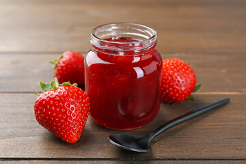 Tasty homemade strawberry jam in glass jar and berries on wooden table, closeup