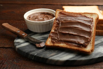 Sandwiches with chocolate butter and knife on wooden table, closeup