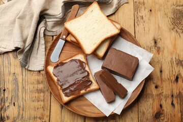 Pieces of tasty chocolate butter, slices of bread and knife on wooden table, top view
