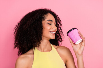 Young woman in stylish yellow dress enjoying leisure moment with coffee against cheerful pink background