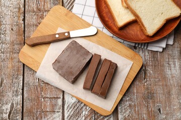 Tasty chocolate butter, slices of bread and knife on wooden table, flat lay