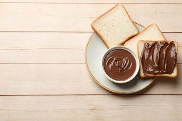 Tasty chocolate butter and slices of bread on light wooden table, top view. Space for text