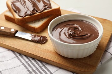 Tasty chocolate butter in bowl, slices of bread and knife on table, closeup