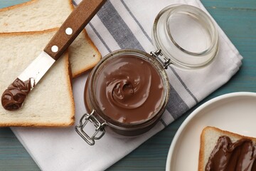 Tasty chocolate butter in jar, knife and slices of bread on light blue wooden table, flat lay