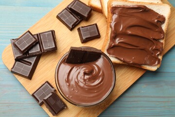 Tasty chocolate butter, pieces and bread on light blue wooden table, top view