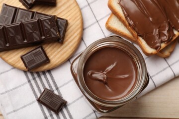 Tasty chocolate butter in jar, pieces and sandwiches on wooden table, top view
