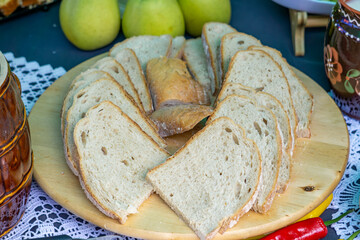 Slices of freshly cut bread arranged on a wooden board, with pears and traditional pottery in the...