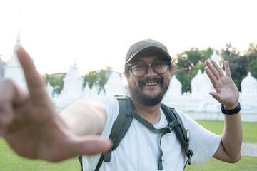 Young Asian man using smartphone to take selfie during solo travel, enjoying adventure and freedom.