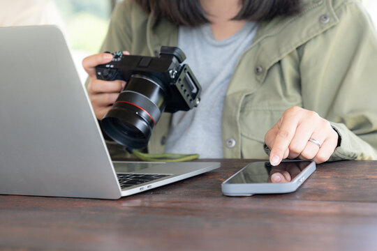 Asian female photographer transferring image files from camera to laptop, working on photo project. - Powered by Adobe