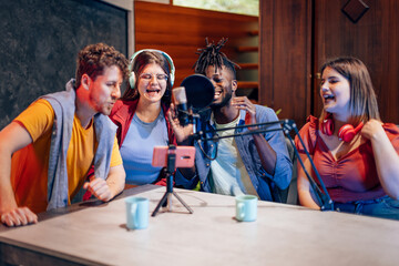 Four happy podcasters laughing while recording audio podcast in home studio