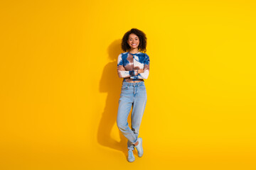 Young stylish female standing confidently against vibrant yellow background, casually dressed with curls
