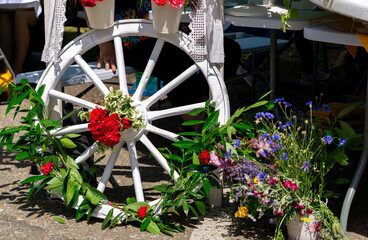 White painted wagon wheel decorated with fresh flowers and green branches, surrounded by colorful...