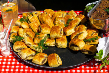 tray of baked puff pastry rolls served on a red and white checkered tablecloth, accompanied by a...