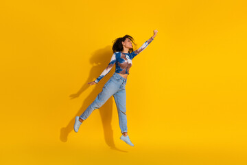 Stylish young woman with curly hair poses confidently, wearing denim and tie-dye top, set against a...