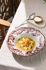 Fish soup with salmon pieces, bright daylight, overhead composition, ornate rimmed plate