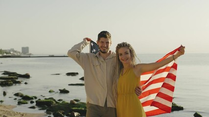 Couple joyfully celebrates with American flag at a beach during sunset, capturing a moment of happiness and unity by the ocean - Powered by Adobe
