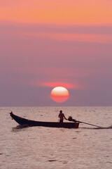 a lone fisherman on a traditional Thai longtail boat sailing on the sea under the setting orange...