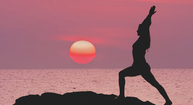 Silhouette of a woman practicing yoga against the background of a purple pink sea sunset. The photo was taken on the Andaman Sea in Thailand, Yoga for travel.
